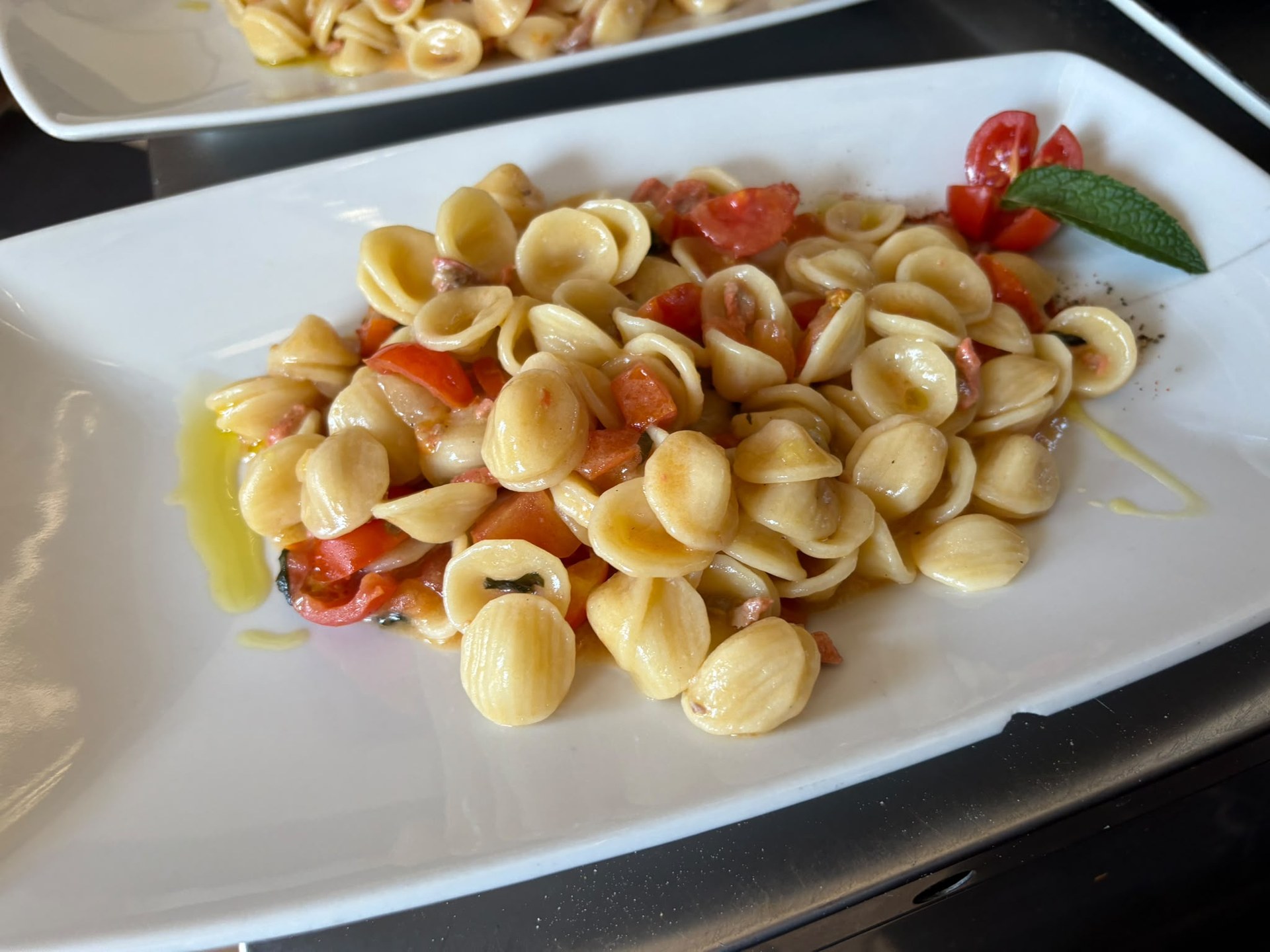 Orecchiette di Dolce Aroma con pomodorini, filo d'olio e foglia di menta su piatto bianco rettangolare