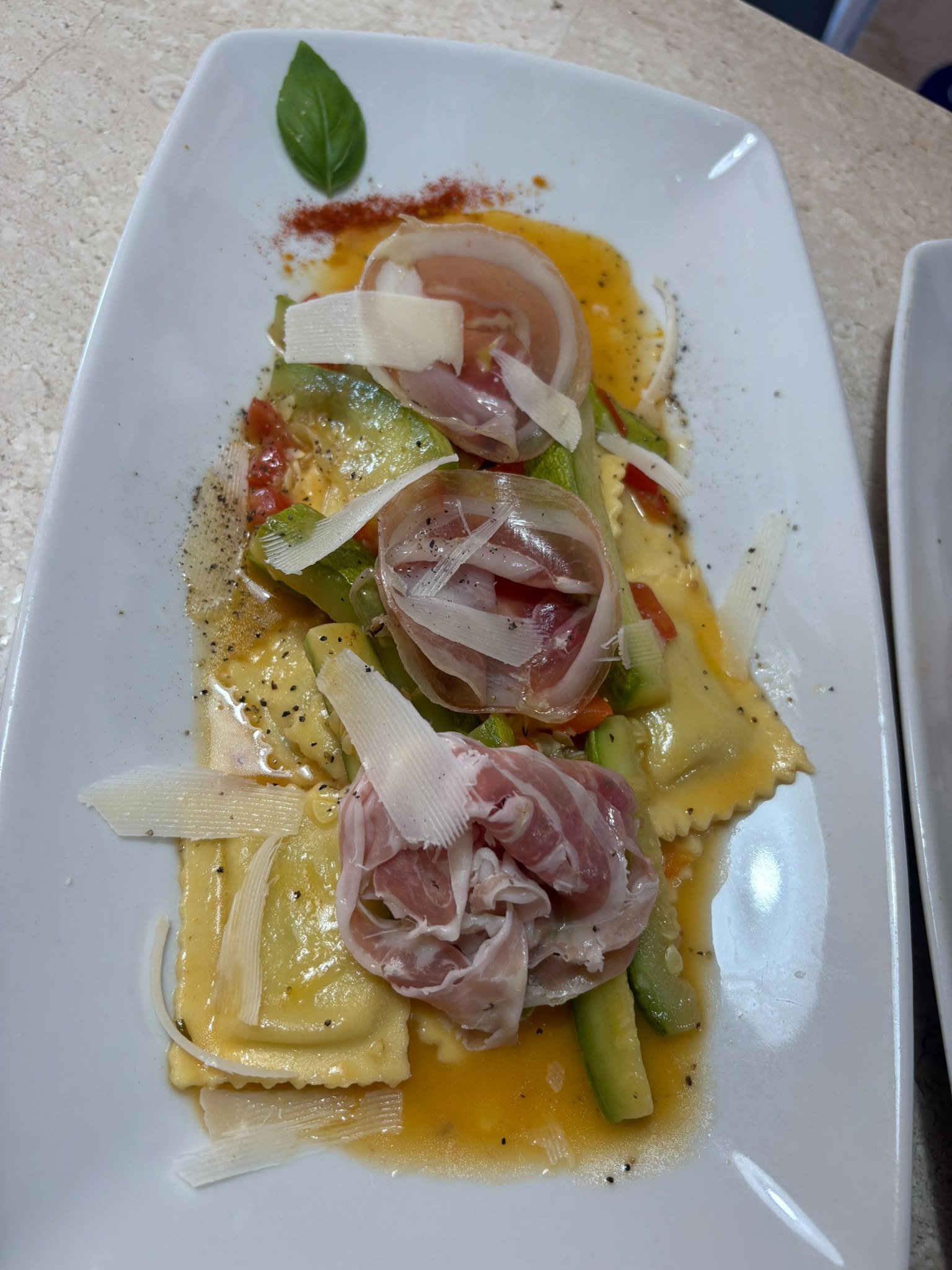 Ravioli con zucchine, pomodorini, prosciutto crudo e scaglie di formaggio su piatto bianco, piatto di Dolce Aroma